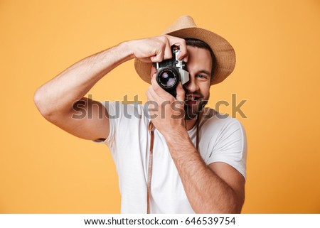 Young man wearing hat and white t-shirt trying to take photo with old camera isolated
