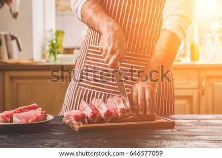 Man cuts of fresh piece of beef on a wooden cutting board in the home kitchen