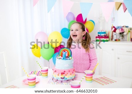Kids birthday party with colorful pastel decoration and unicorn rainbow cake. Little girl with sweets, candy and fruit. Balloons and banner at festive decorated table for child or baby birthday party.