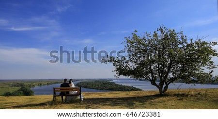 Young wedding romantic couple sitting on wooden bench outdoor on natural background, horizontal picture. copy space.
