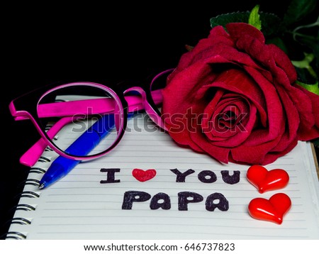 Father's day concept. I LOVE PAPA message write on note book with red rose, glasses and two red hearts on dark background