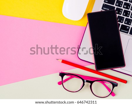 Top view of smartphone on laptop, mouse, glasses and pencil on pink, yellow and green and yellow background