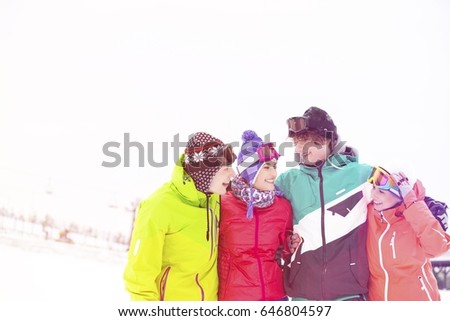 Cheerful young friends standing arm around in snow