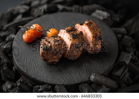 Meat - steak and tomatoes on a wooden board on coals. Close-up on a black background. Healthy delicious food.