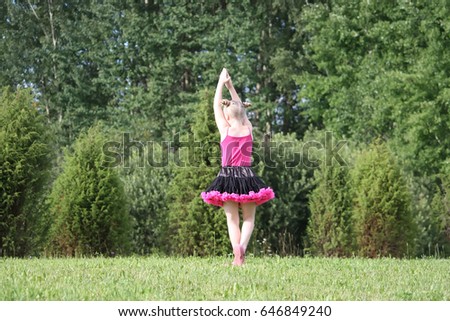 Adorable blonde girl dressed in a tutu skirt dancing in a summer park in the countryside.