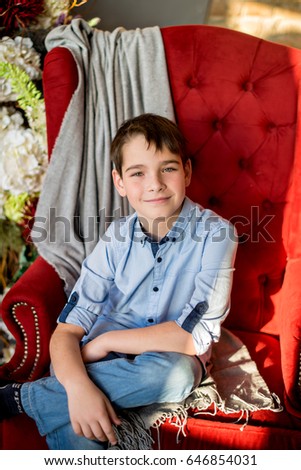 Portrait of a smile brunet teenage boy sitting on a red armchair. Close up