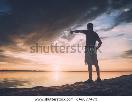Man standing on the beach near the beach and points to the west. Sunset time. Instagram stylization.