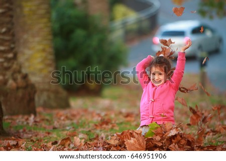 outdoor portrait of young happy child girl playing with autumn leaves in park on natural background