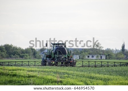 Tractor with high wheels is making fertilizer on young wheat. The use of finely dispersed spray chemicals. Tractor with a spray device for finely dispersed fertilizer. Tractor on sunset background.