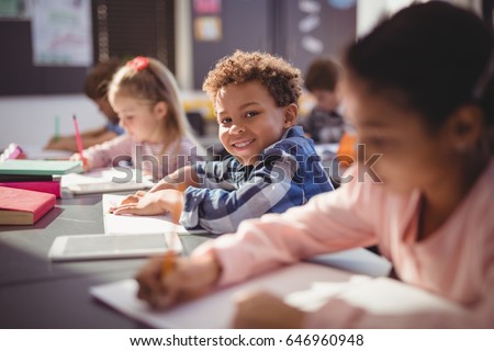 Portrait of smiling schoolboy doing his homework in classroom at school Royalty-Free Stock Photo #646960948