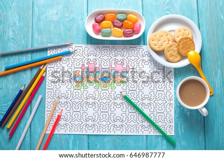 White sheet of paper, coloring for adults for rest and relaxation. Blue vintage background, painted wood. Colour pencils. multicolored candies in a saucer and a cup of coffee with milk.