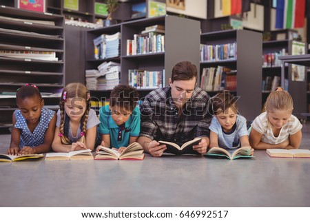 Teacher and schoolkids lying on floor while reading books in library at school