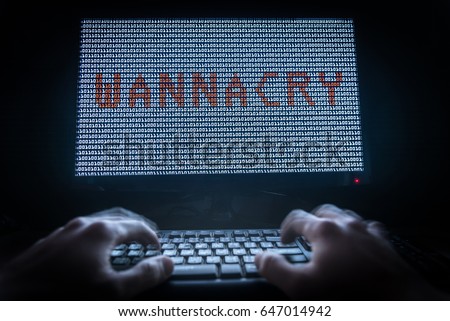 The hacker is developing the wannacry malware in the darkness. The developer typing the keyboard in the front of the screen.