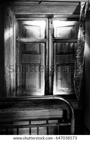 The room is a retro. The old window with closed shutters. In the foreground is an iron bed. Photographed in the Cherkassy region. Ukraine. Black and white image.