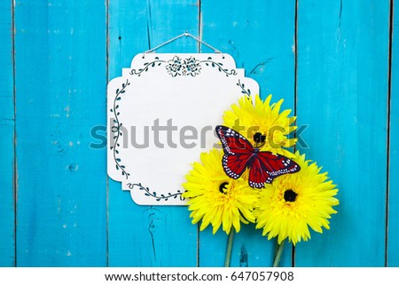 Blank wood sign with red butterfly and yellow flowers hanging on antique rustic teal blue wooden door; springtime, Mothers Day, family, Memorial Day holiday background with white copy space