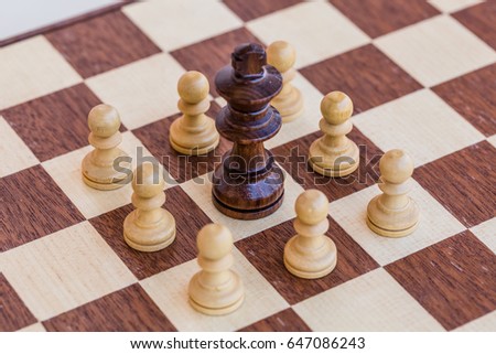 chess game. abstract composition of chess figures in chessboard isolated on light background. black king surrounded white pawns. top view
