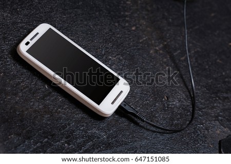 Plugged cellphone on the dark texture