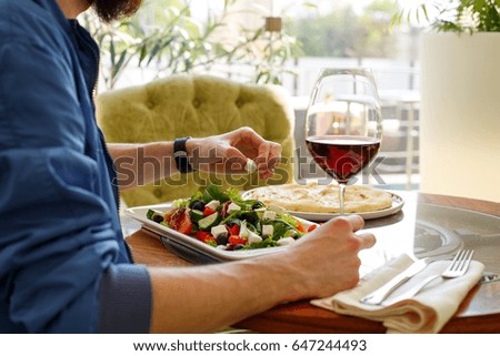 Man with glass of wine in one hand. Silhouette of a man with glass of wine in one hand and menu in other hand in the restaurant with blurred background. Plate of green salad on the table