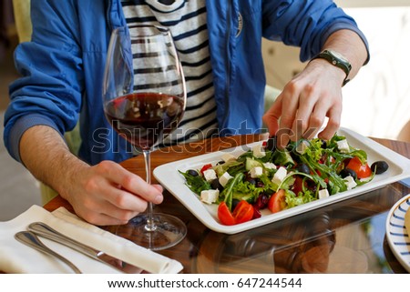 Man with glass of wine in one hand. Silhouette of a man with glass of wine in one hand and menu in other hand in the restaurant with blurred background. Plate of green salad on the table