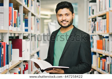 Happy indian male student at the library Royalty-Free Stock Photo #647258422