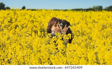 Woman with dog on arms in a rape field.