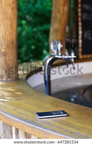 Someone lost a cell phone in a garden pub. Forgotten smartphone on a bar counter in the outdoor restaurant. Beer draft in a background.