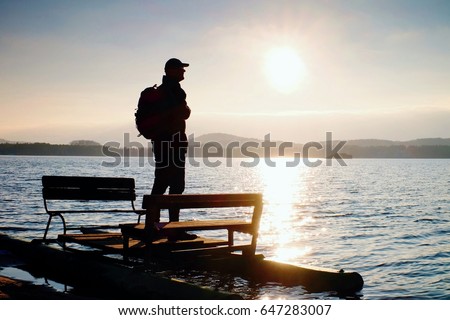 Tall tourist with backpack walk on beach at abandoned  pedal boat in the sunset. Autumn sunny day  at sea