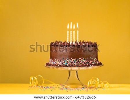 Chocolate birthday cake with sprinkles and candles over yellow background.