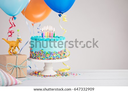 Childs dinosaur themed birthday party with blue cake and colorful balloons over light grey.