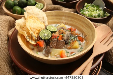Soto Betawi. Traditional beef and offal soup from Betawi, Jakarta. The soup has been preplated in a bowl; ready to be served. It is surrounded by some of the condiments. Royalty-Free Stock Photo #647350303