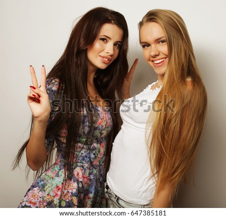 Two young girl friends standing together and having fun. Over white background.
