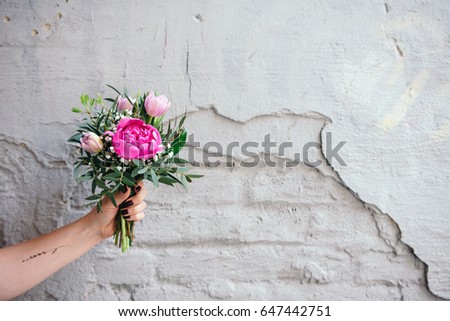 Small bouquet of peonies, tulips flowers in a woman's hand on brick wall  with free space