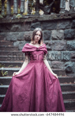 Young princess in lilac dress walking through the yard of ancient castle.