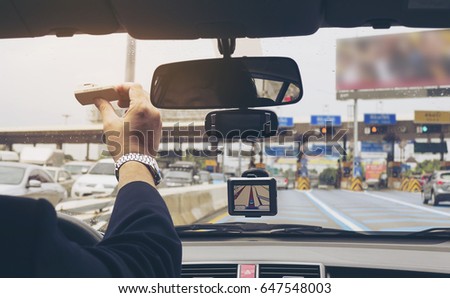 Man driving car using navigator and holding electronic toll collection system device Royalty-Free Stock Photo #647548003
