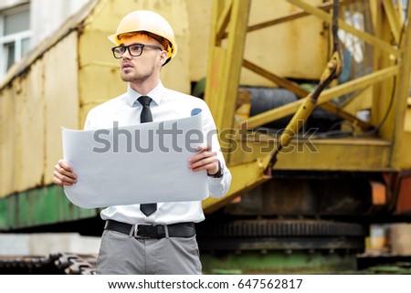 Engineer builder in a helmet holds drawings at construction site