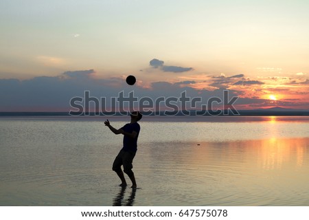 Silhouette of young man playing football or soccer at the beach with beautiful sunset background Childhood, serenity, sport, lifestyle concept.