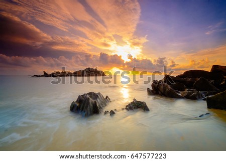 Soft wave with rocks foreground  on the sandy beach. Natural sunrise and rock island as background at Pantai Penunjuk ,Malaysia. Image contain grain and motion blur effect.
