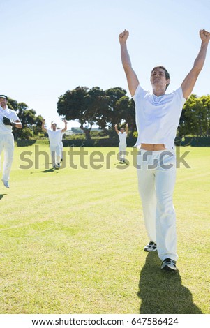 Happy cricket players enjoying victory while standing on field against clear sky