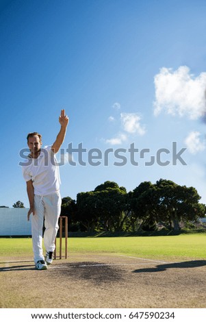 Full length of man bowling while standing on cricket field against sky