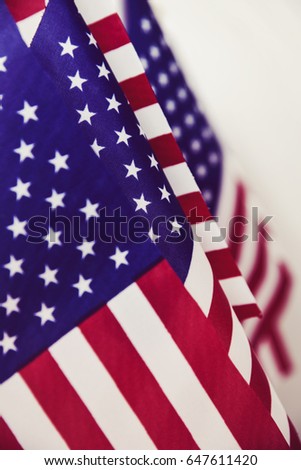 closeup of many american flags put in line, against an off-white background