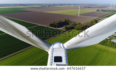 Aerial photo close up of wind turbine showing dirty blades pointing upwards mill located on grassland also showing more aerofoil powered windmills providing sustainable energy Royalty-Free Stock Photo #647616637