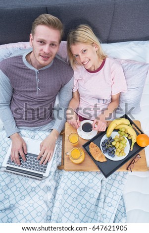 Picture of young couple eating breakfast and working on laptop in bed      