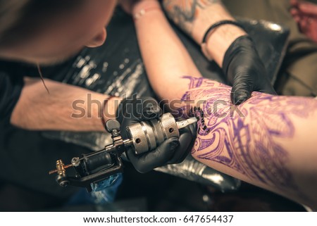 Top view of special device which keeping male. He making tattoo on arm of client