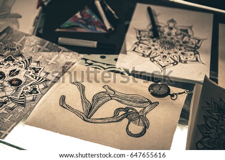 Time does not dominate over picture. Various sketches of tattoos locating on desk in salon. Close up