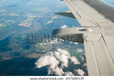 Fields and forests under the wing of the aircraft, the view from the window of an airplane, travel in the plane
