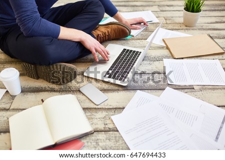 Unrecognizable student  sitting cross legged on wooden floor, using laptop computer while studying and preparing for exams Royalty-Free Stock Photo #647694433