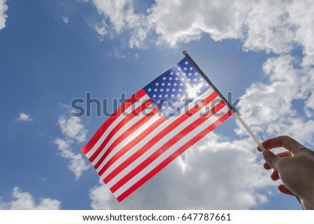 Hand holding american flag close up against blue sky with clouds