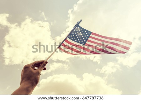 Hand holding american flag close up against blue sky with clouds