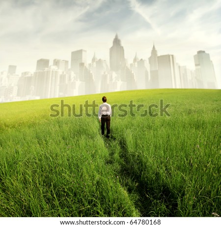 Businessman walking on a green meadow with cityscape on the background Royalty-Free Stock Photo #64780168