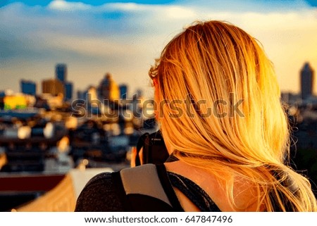 Blonde girl taking picture of city centre when sun goes down